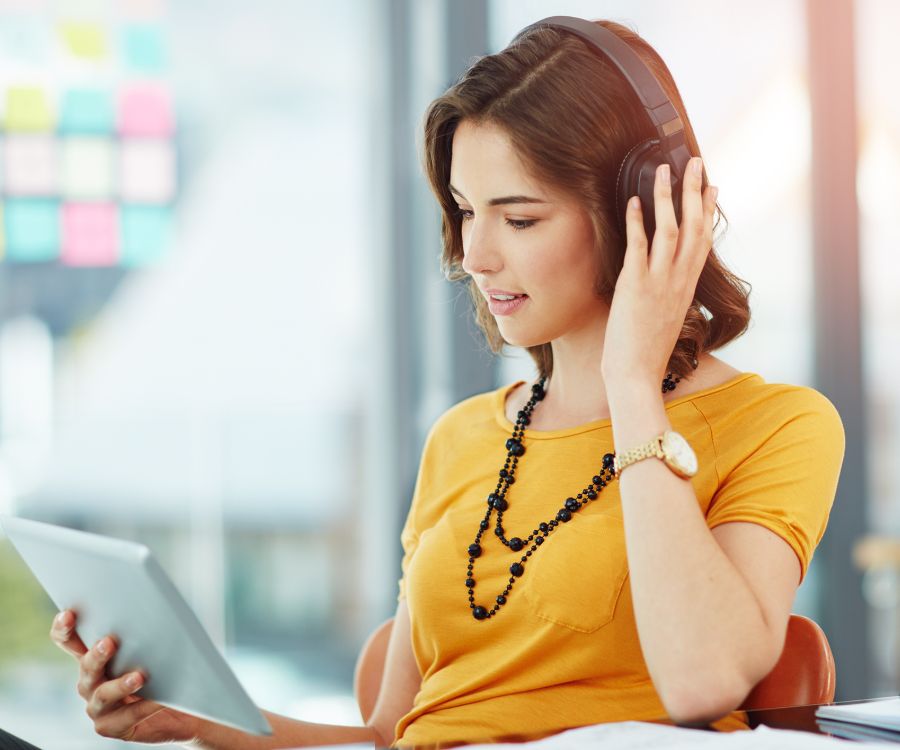 Image of a woman wearing headphones as she attends to an online learning session viewed on her tablet device.