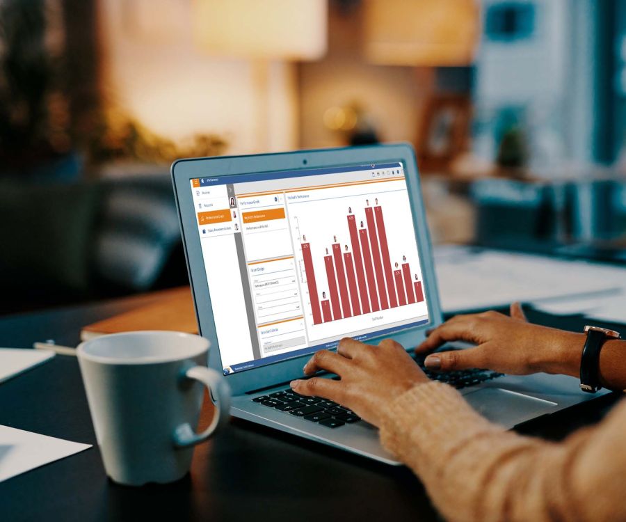 Woman seated at a desk viewing the Performance Management module interface by Frontier Software. A coffee cup is in the right hand foreground