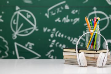 Headphones on a stack of books with a jar of colored pencils, in front of a chalkboard with math formulas.