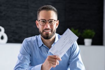 Man in blue shirt in office holding pay related document.