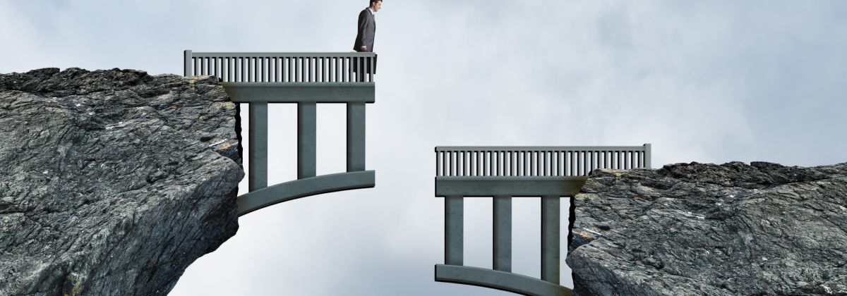 Businessman stands on a broken bridge between two cliffs, facing a dangerous gap.